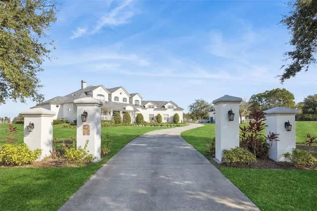 a view of a white house with a big yard plants and large trees