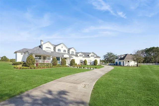 a view of a white house with a big yard plants and large trees