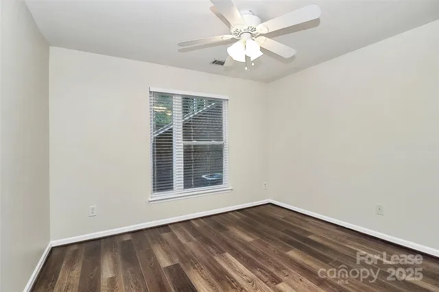an empty room with wooden floor chandelier fan and windows