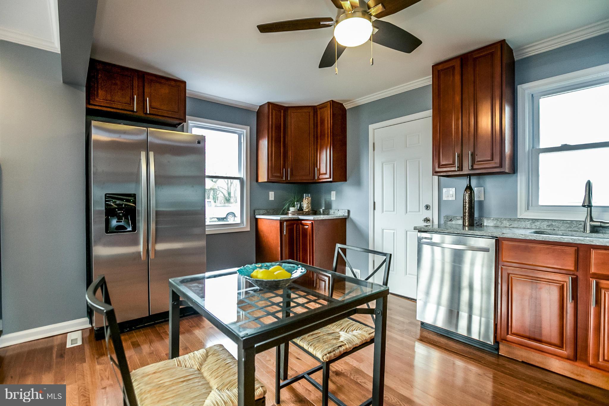 3534 Milford Mill Road Baltimore, MD 21244 - Photo 7 of 30 a kitchen with stainless steel appliances granite countertop a stove top oven a refrigerator and a dining table with wooden floor