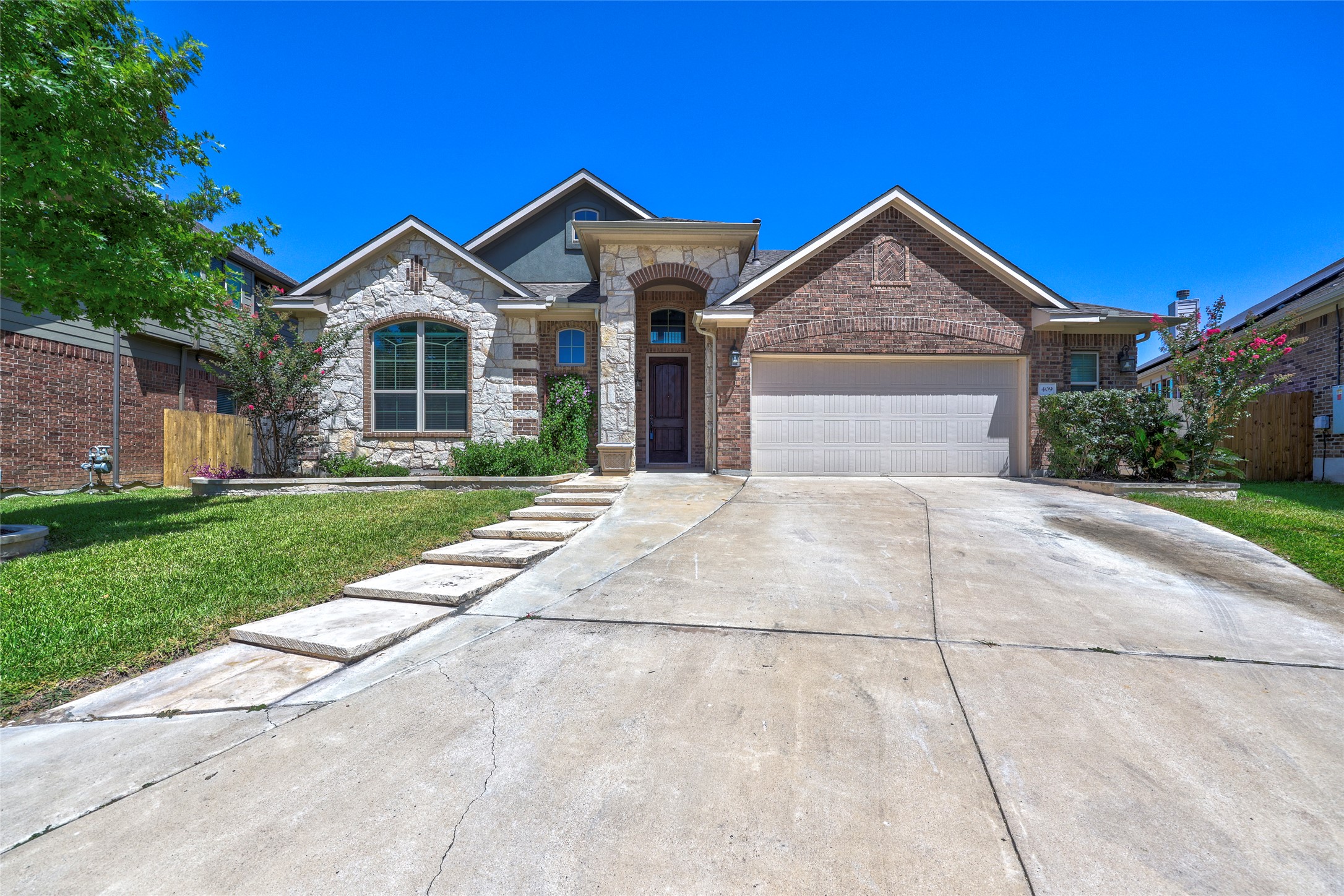 409 Betony Loop Buda, TX 78610 - Photo 2 of 38 A well-kept front yard and a concrete driveway lead to this appealing brick and stone home.