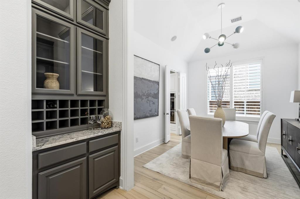 1933 Snapdragon Road Frisco, TX 75033 - Photo 6 of 40 Built-in cabinetry with glass-front uppers and wine storage, light-toned wood-finish flooring, vaulted ceiling, and window with plantation shutters