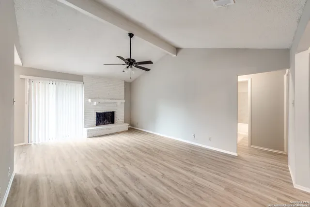 a view of an empty room with wooden floor fireplace and a window