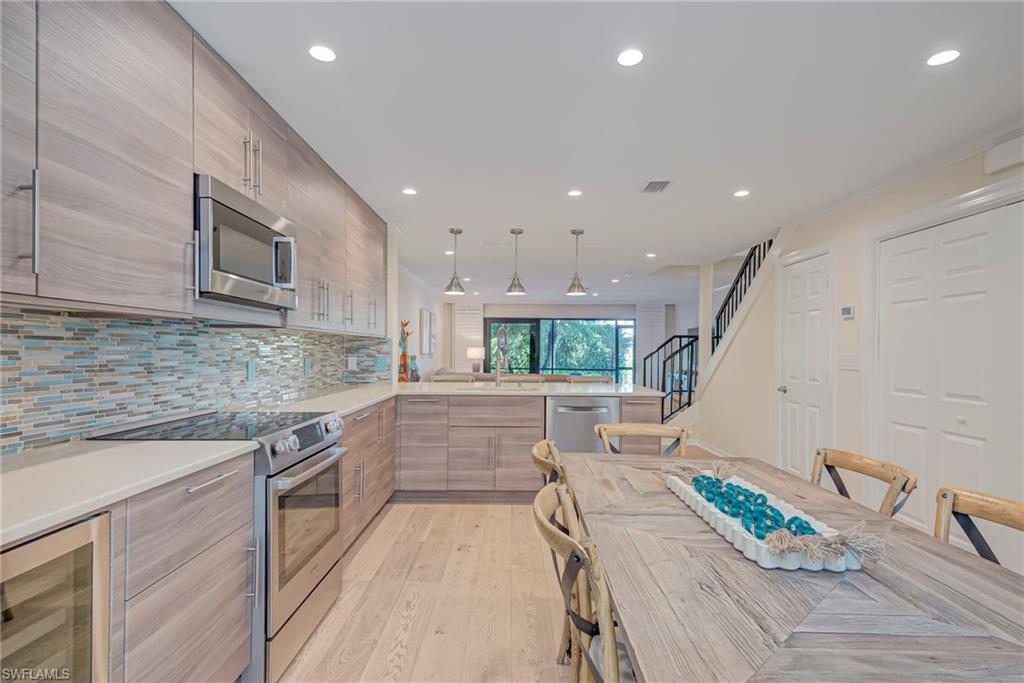 1070 6th Street South, Unit 1070 Naples, FL 34102 - Photo 10 of 41 Kitchen featuring stainless steel appliances, modern cabinets, wine cooler, pendant lighting, and light stone countertops. There is a large walk-in pantry/storage closet and full washer and dryer ( on right). Guest bathroom is to the right as well.