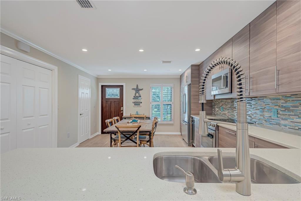1070 6th Street South, Unit 1070 Naples, FL 34102 - Photo 13 of 41 Kitchen with light stone countertops, stainless steel appliances, light wood-style flooring, tasteful backsplash, and ornamental molding. To the left in the picture ( closest to front door) is the guest bathroom and full size washer and dryer closet.
