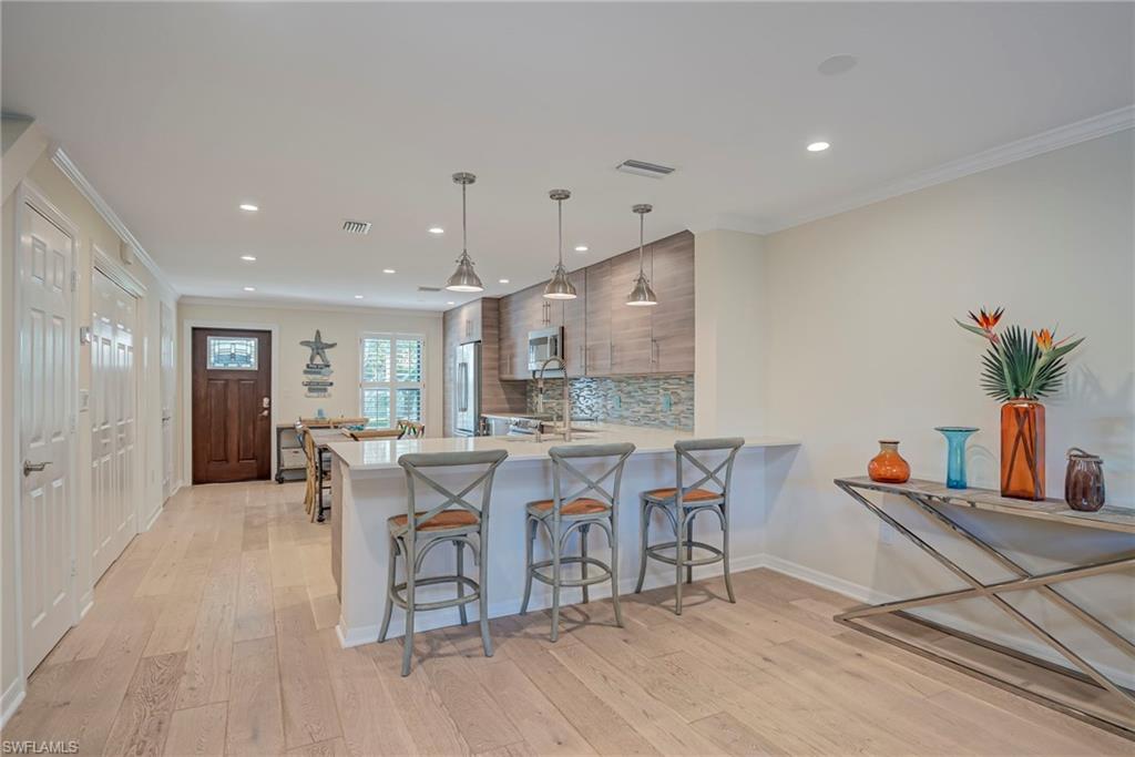 1070 6th Street South, Unit 1070 Naples, FL 34102 - Photo 20 of 41 Kitchen featuring a breakfast bar, ornamental molding, light stone countertops, hanging light fixtures, and plenty of space!