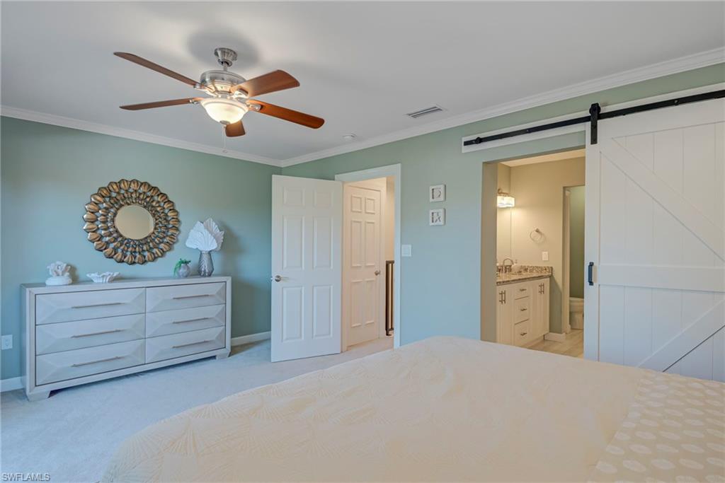 1070 6th Street South, Unit 1070 Naples, FL 34102 - Photo 31 of 41 Bedroom featuring crown molding, a barn door, ceiling fan, light colored carpet, and ensuite bathroom featuring a barn door entry - double vanity, walk-in closet, and walk-in shower, toilet