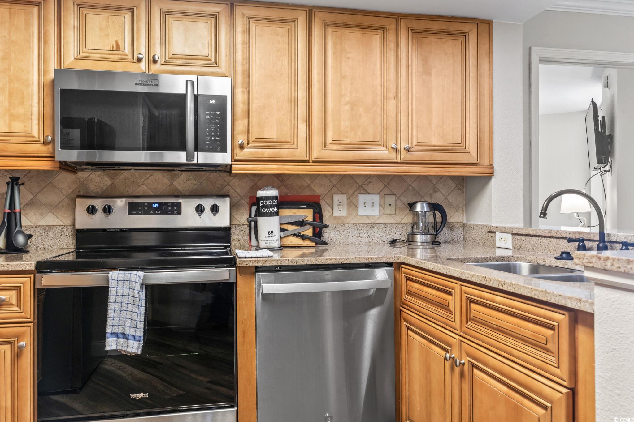7100 North Ocean Boulevard, Unit 616 Myrtle Beach, SC 29572 - Photo 2 of 23 Kitchen featuring stainless steel appliances, light stone counters, brown cabinets, and decorative backsplash