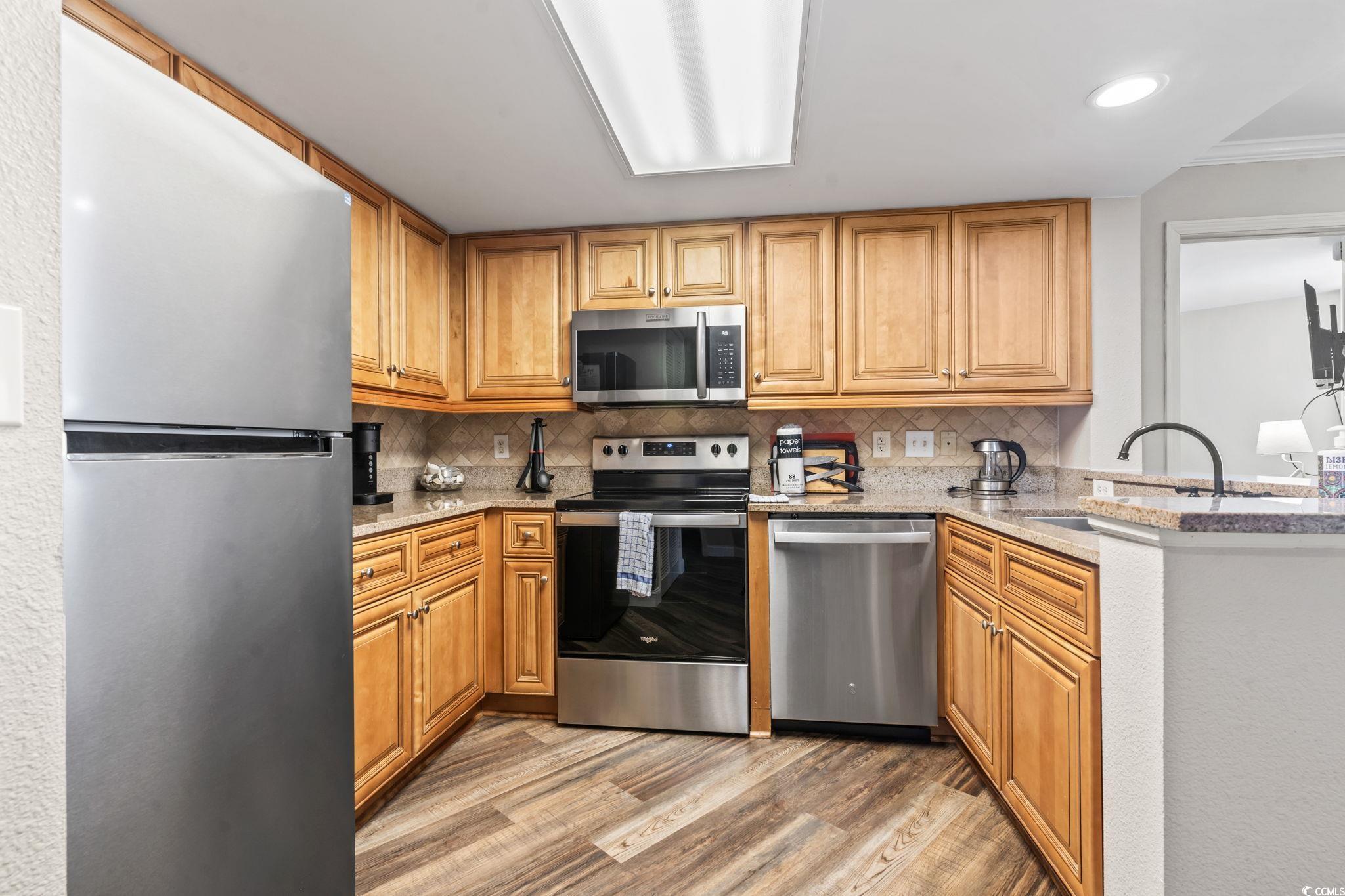 7100 North Ocean Boulevard, Unit 616 Myrtle Beach, SC 29572 - Photo 3 of 23 Kitchen with stainless steel appliances, light stone countertops, backsplash, light wood-style floors, and brown cabinetry