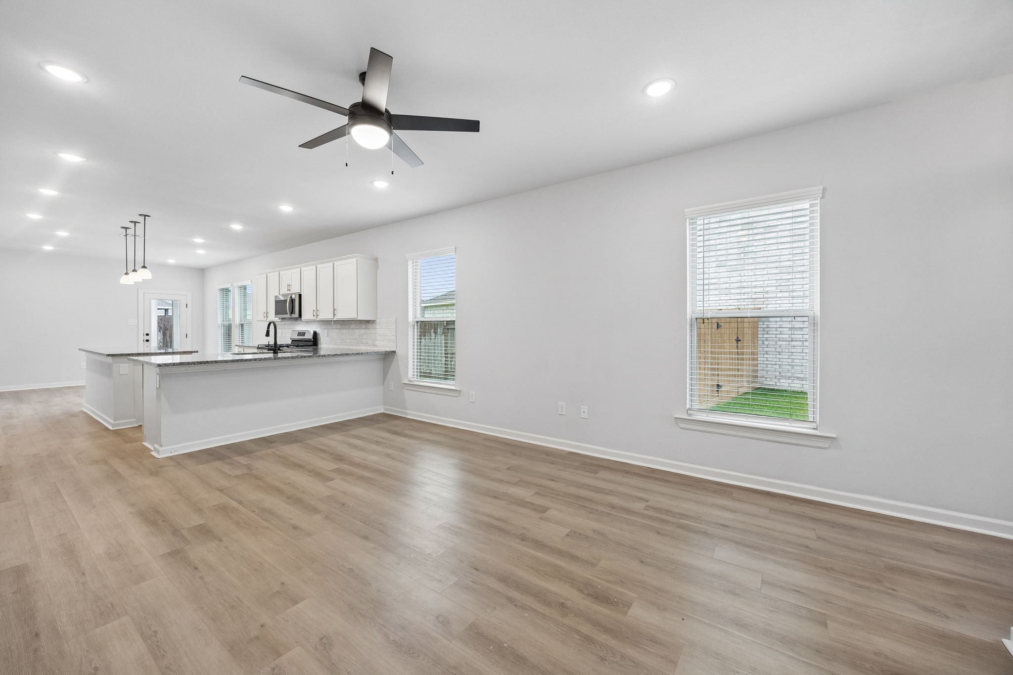10902 Bonfire Trail Beasley, TX 77417 - Photo 5 of 36 This photo showcases a spacious, open-plan kitchen and living area with modern finishes. It features light vinyl plank flooring, a large kitchen island with granite countertops, white cabinetry, stainless steel appliances, and ample natural light from multiple windows. A ceiling fan and recessed lighting provide a bright, airy atmosphere.