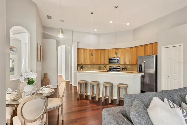 a kitchen with stainless steel appliances granite countertop a refrigerator a stove a kitchen island with couches chairs and wooden floor