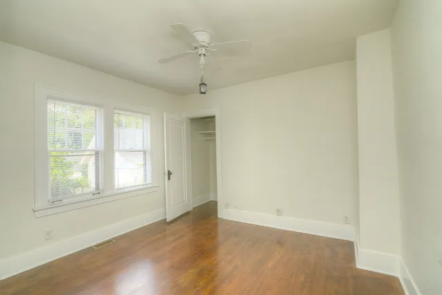 an empty room with wooden floor fan and windows