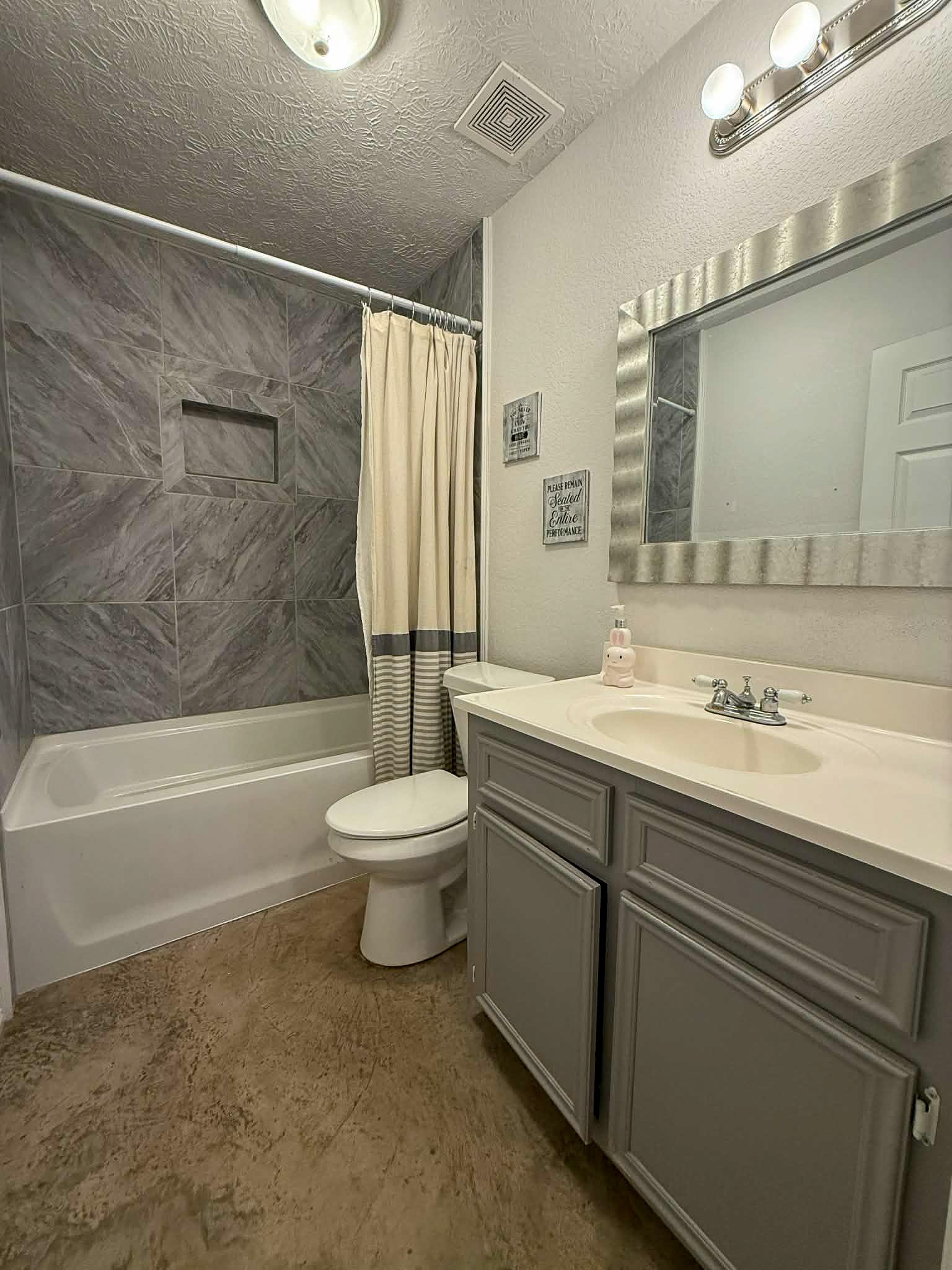 107 County Road 409 Sweeny, TX 77480 - Photo 13 of 20 Cozy bathroom with modern gray cabinets and a sleek countertop. Features a bathtub with elegant tile surround, a large mirror, and stylish lighting. Perfect for relaxing and freshening up.