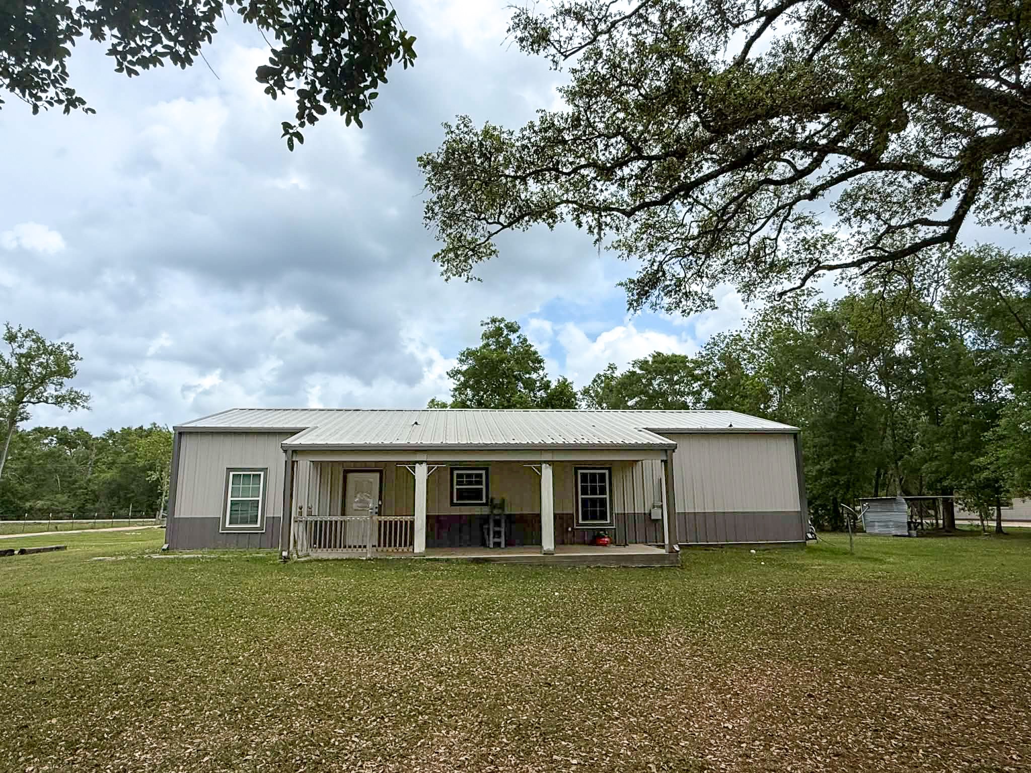 107 County Road 409 Sweeny, TX 77480 - Photo 17 of 20 This property features a charming single-story home with a cozy back patio, set on a spacious grassy lot surrounded by mature trees, offering a serene and private environment.