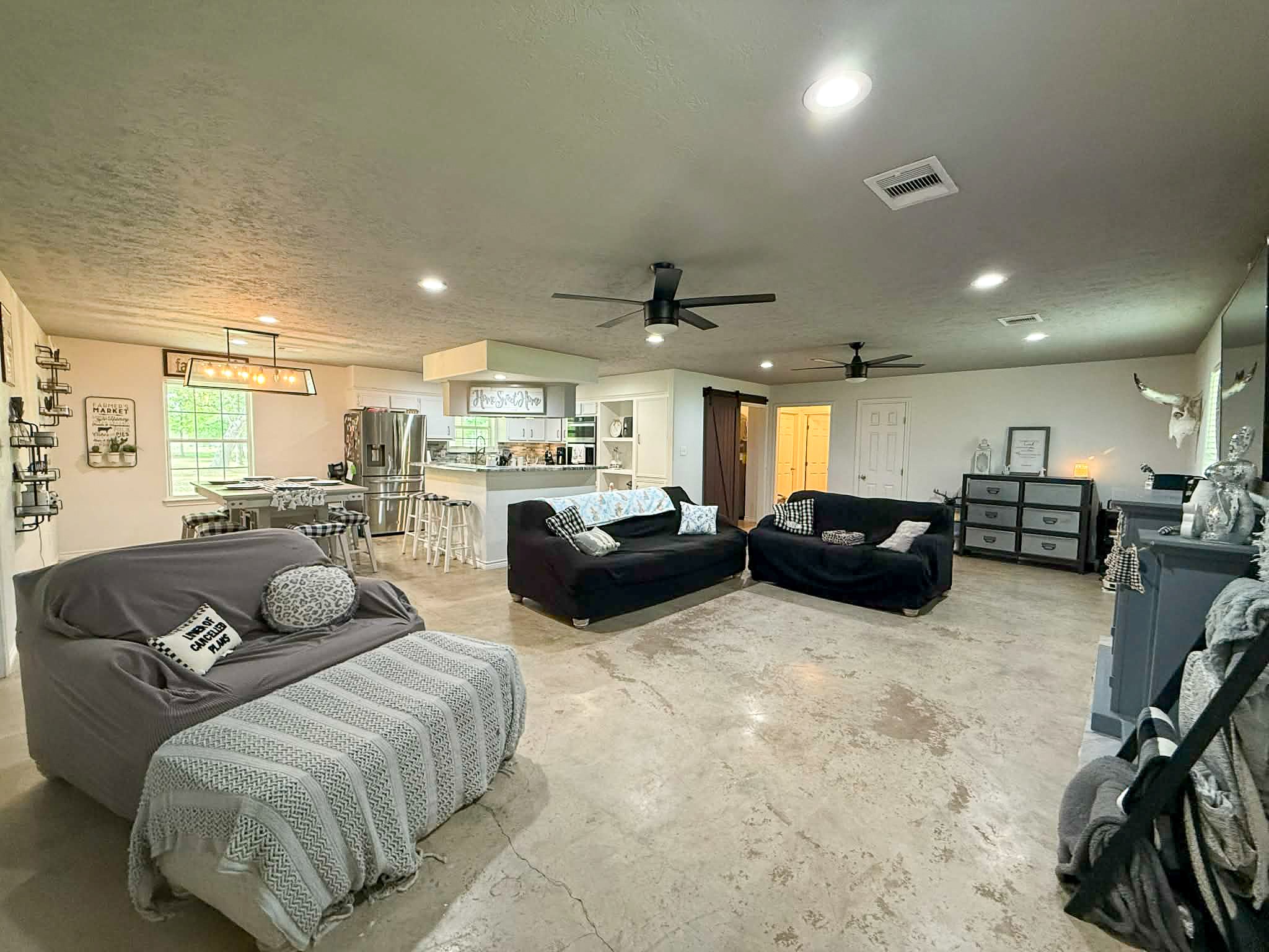 107 County Road 409 Sweeny, TX 77480 - Photo 3 of 20 Spacious open-concept living area with polished concrete floors, modern ceiling fans, and ample natural light. The kitchen features a breakfast bar and stainless steel appliances. Cozy seating areas and a dining space complete the inviting atmosphere.