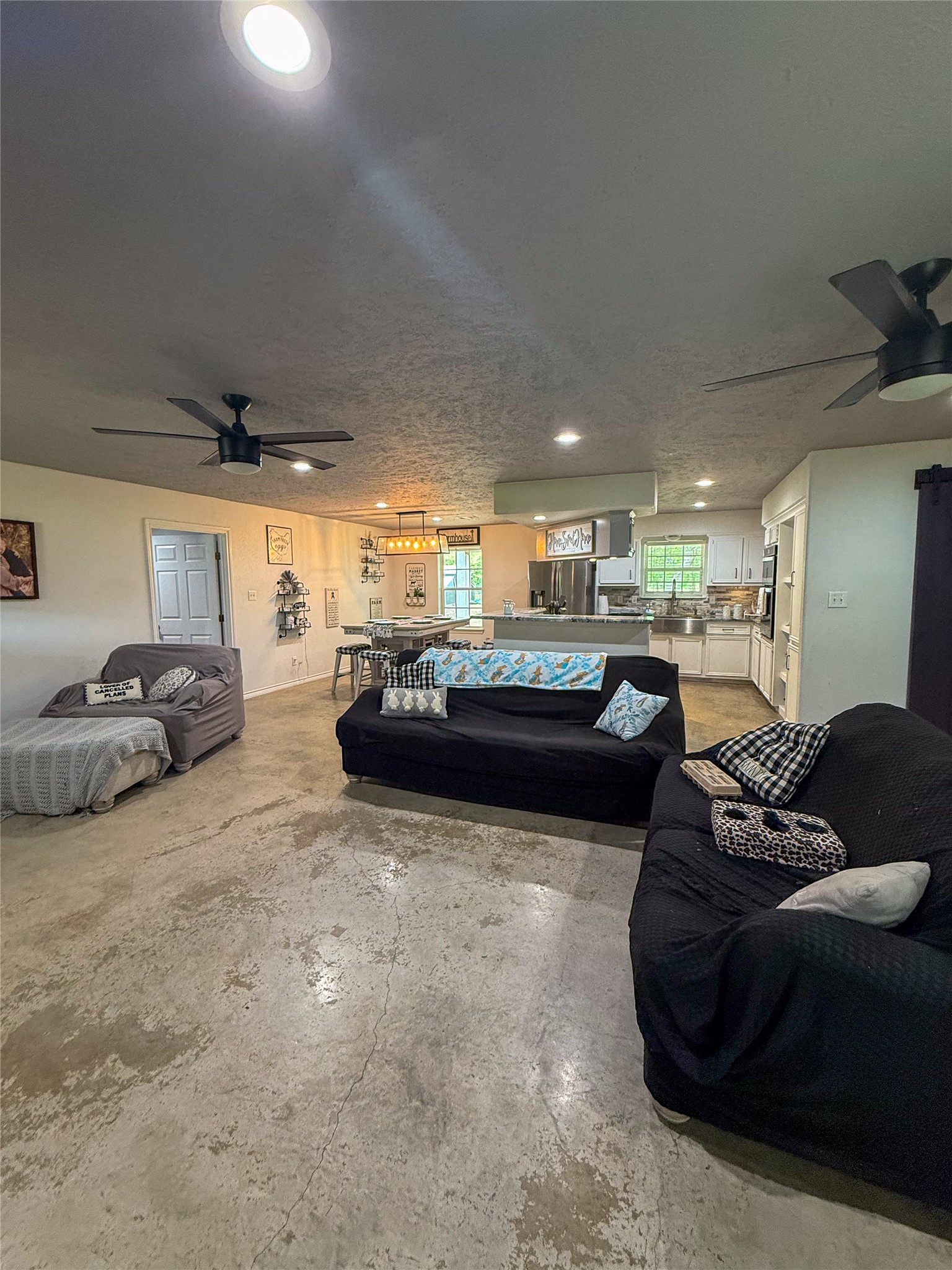 107 County Road 409 Sweeny, TX 77480 - Photo 4 of 20 This spacious open-concept living area features concrete floors, modern ceiling fans, and ample natural light. The room seamlessly connects to a stylish kitchen with stainless steel appliances, ideal for entertaining or family gatherings.