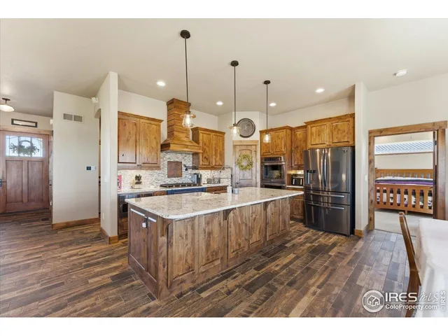 a large kitchen with stainless steel appliances a large counter top a stove a refrigerator and a wooden floor