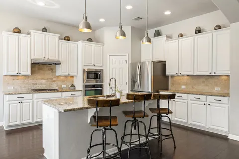 a kitchen with stainless steel appliances kitchen island granite countertop a table chairs microwave and sink