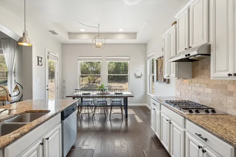 a kitchen with granite countertop a stove a sink a refrigerator dining table and chairs with wooden floor