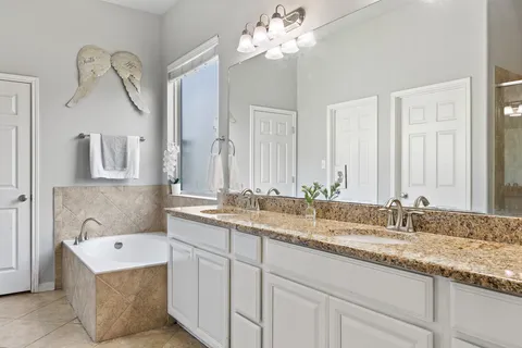a bathroom with a granite countertop double vanity sink and mirror with bathtub