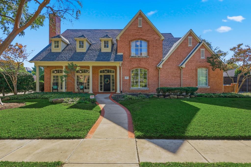 View of front of house with a front lawn, covered porch, brick siding, and a chimney