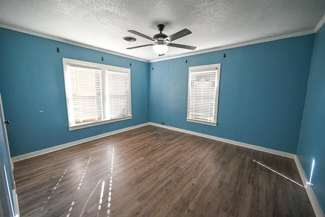 an empty room with wooden floor chandelier fan and windows