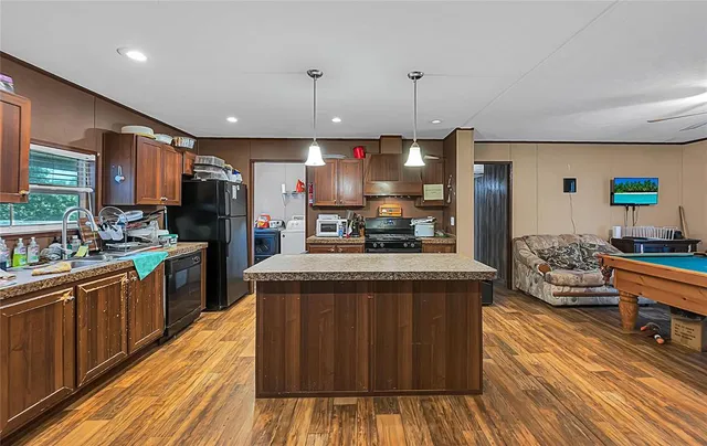 a kitchen with stainless steel appliances granite countertop a stove a sink dishwasher a refrigerator and a dining table with wooden floor