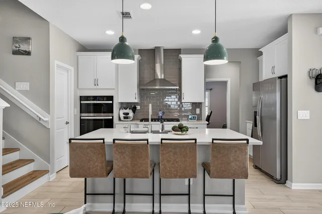 a kitchen with stainless steel appliances kitchen island granite countertop a dining table chairs refrigerator and cabinets