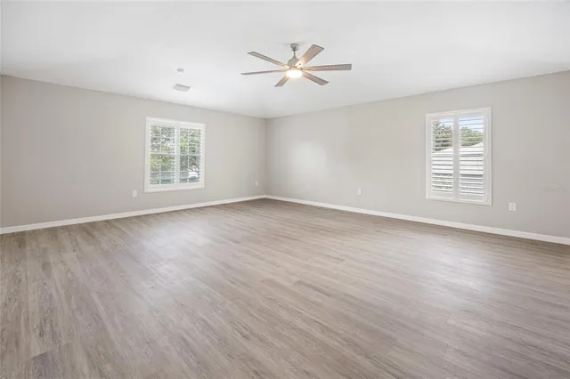 an empty room with wooden floor fan and windows
