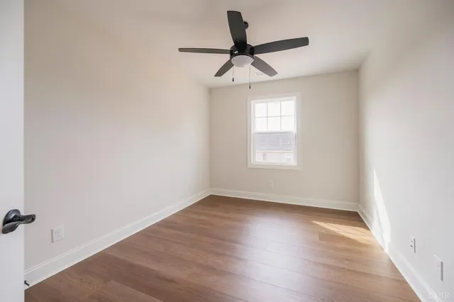 an empty room with wooden floor ceiling fan and windows