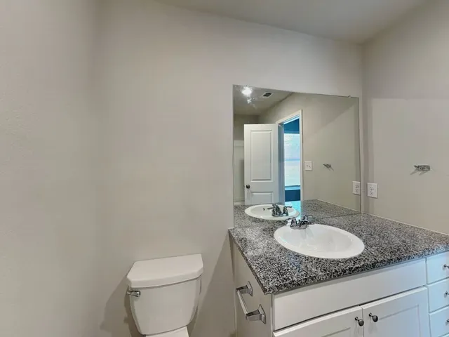 a bathroom with a granite countertop sink a toilet and a mirror