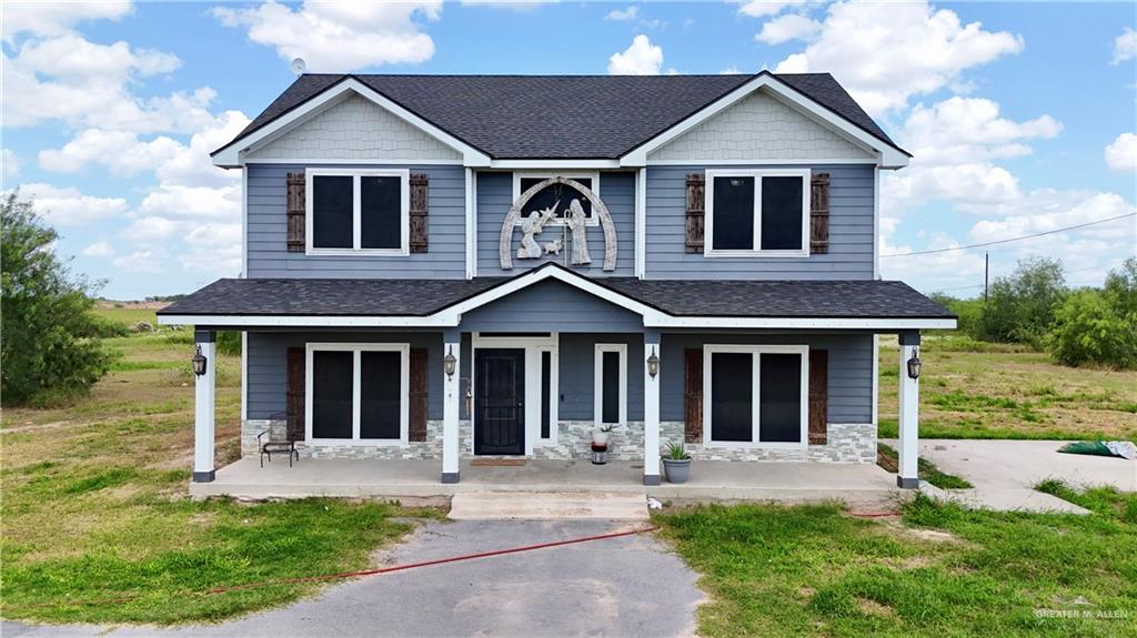 View of front facade with roof with shingles, a porch, and stone siding