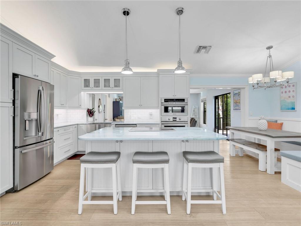 188 Columbus Way Marco Island, FL 34145 - Photo 7 of 38 Kitchen with appliances with stainless steel finishes, glass insert cabinets, decorative light fixtures, a breakfast bar area, and white cabinets