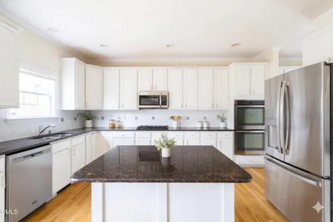 a kitchen with stainless steel appliances kitchen island granite countertop a refrigerator a stove a sink a dining table and chairs with wooden floor