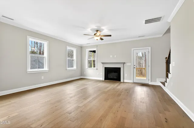a view of an empty room with wooden floor and a kitchen