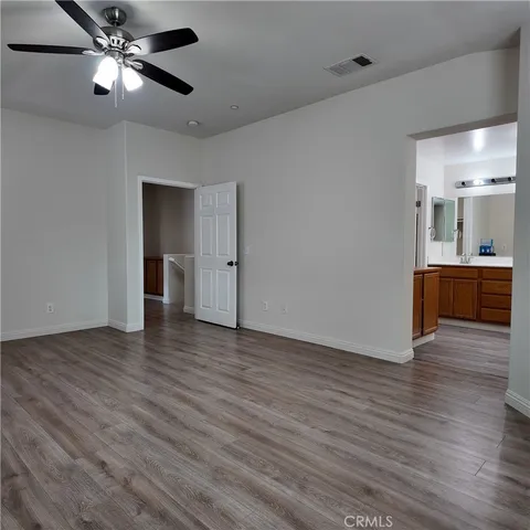 a view of an empty room with wooden floor and a ceiling fan