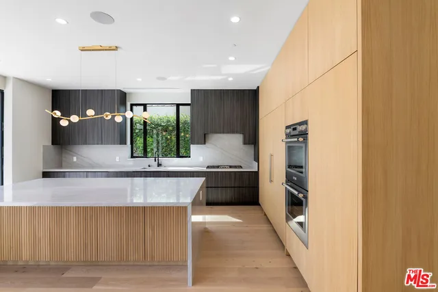 a large kitchen with stainless steel appliances a large counter top a stove a chimney a sink and a refrigerator