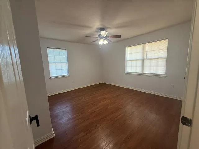 an empty room with wooden floor ceiling fan and windows