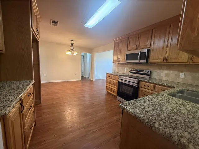 a kitchen with stainless steel appliances granite countertop a stove a sink dishwasher a microwave oven and a refrigerator with wooden floor