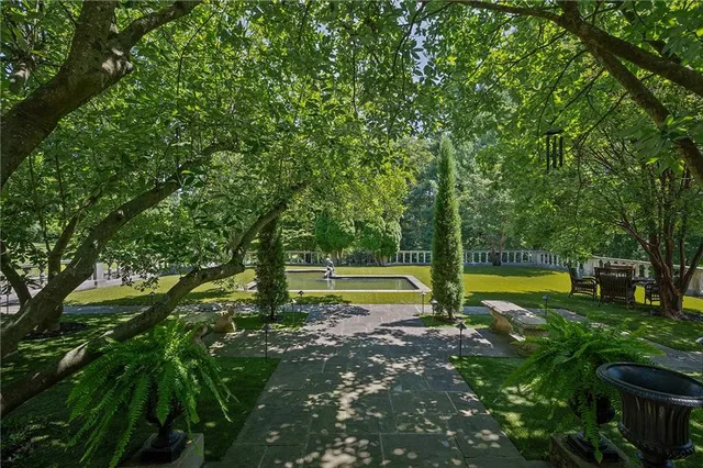 a view of pool with lawn chairs and large trees