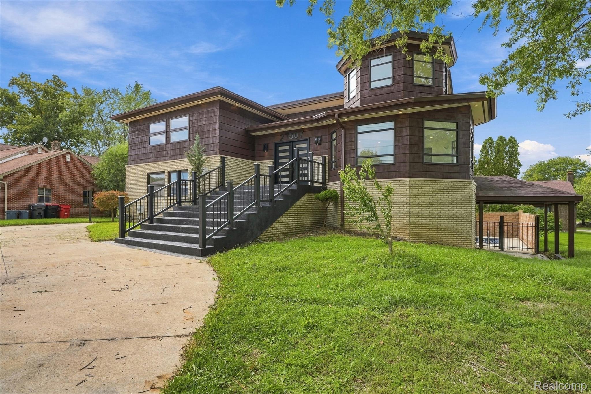27507 Bell Road Southfield, MI 48034 - Photo 5 of 81 Split-level residence featuring a prominent central staircase with black railings, a multi-story octagonal tower, and a covered patio area with a fence