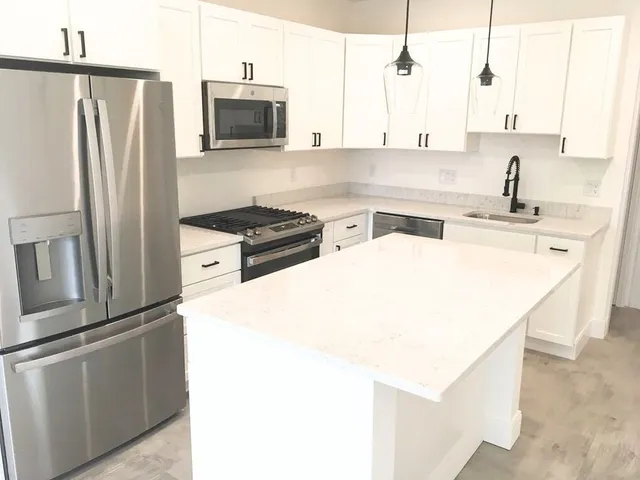 a kitchen with stainless steel appliances a refrigerator a stove a sink and white cabinets