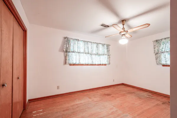 an empty room with wooden floor chandelier fan and windows