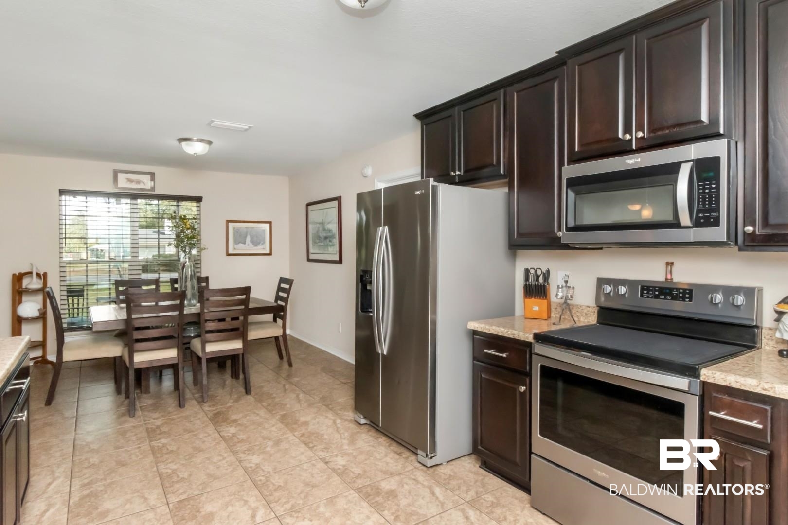 11528 Mocking Bird Lane Fairhope, AL 36532 - Photo 17 of 45 Kitchen with stainless steel appliances, dark wood finish cabinets, light stone counters, and light tile patterned flooring