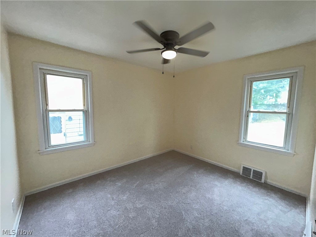 9316 Alexander Road Garfield Heights, OH 44125 - Photo 10 of 27 Bright, light-filled bedroom featuring two large double-hung windows with natural light exposure, neutral wall finishes, neutral carpet flooring, and a ceiling fan with integrated lighting