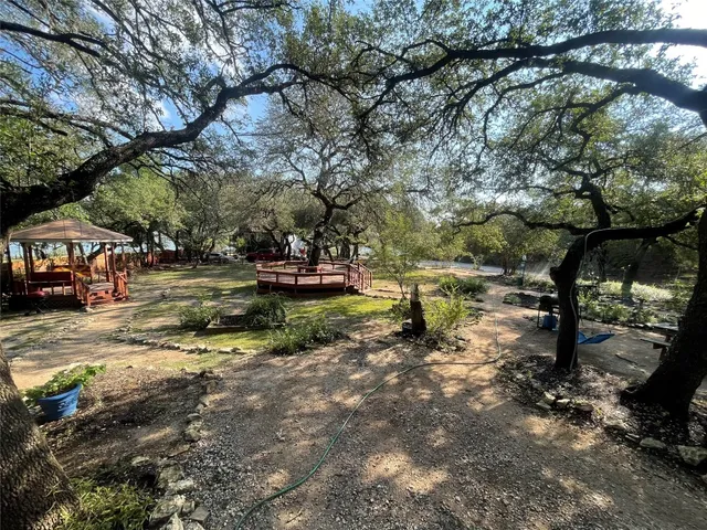 a backyard of a house with table and chairs under an large trees