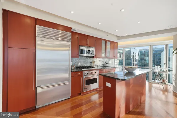 a kitchen with stainless steel appliances granite countertop a refrigerator a sink dishwasher a stove and white countertops with wooden floor