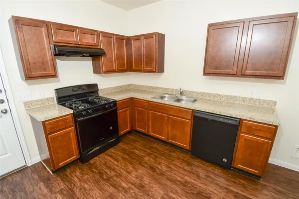 a kitchen with stainless steel appliances granite countertop wooden cabinets a stove a sink and a wooden floor
