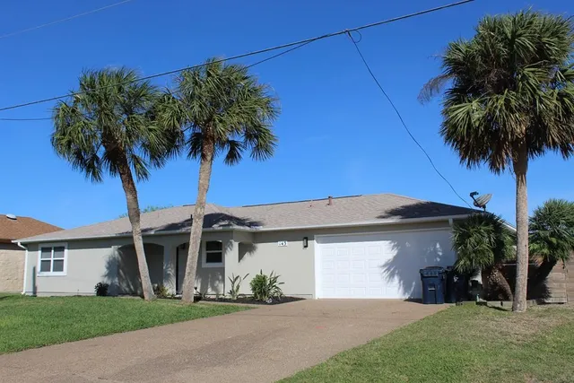 a front view of a house with a garden and palm trees