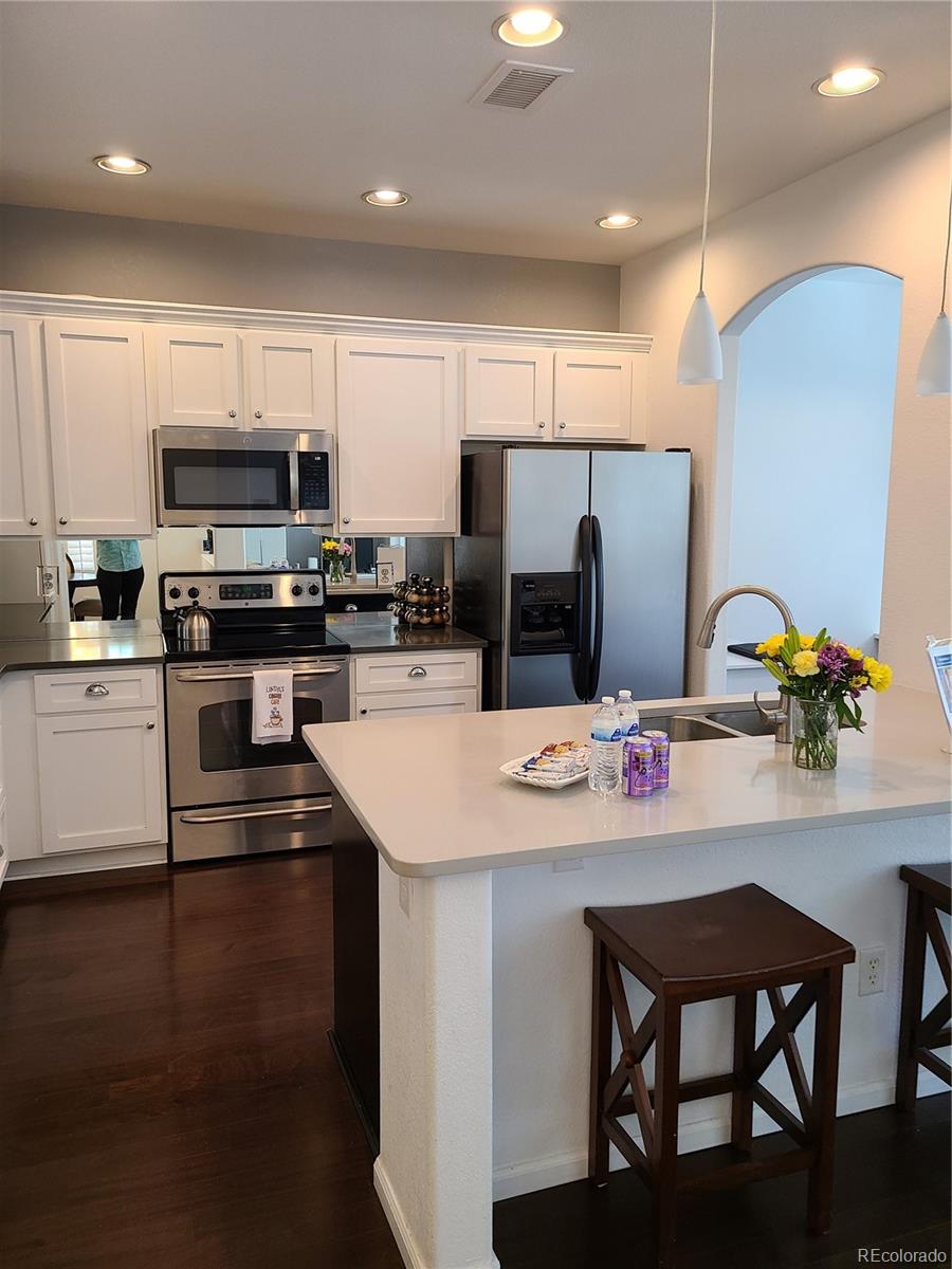 9492 Cedarhurst Lane, Unit B Highlands Ranch, CO 80129 - Photo 5 of 17 a kitchen with stainless steel appliances a stove a sink a microwave a refrigerator and white cabinets with wooden floor